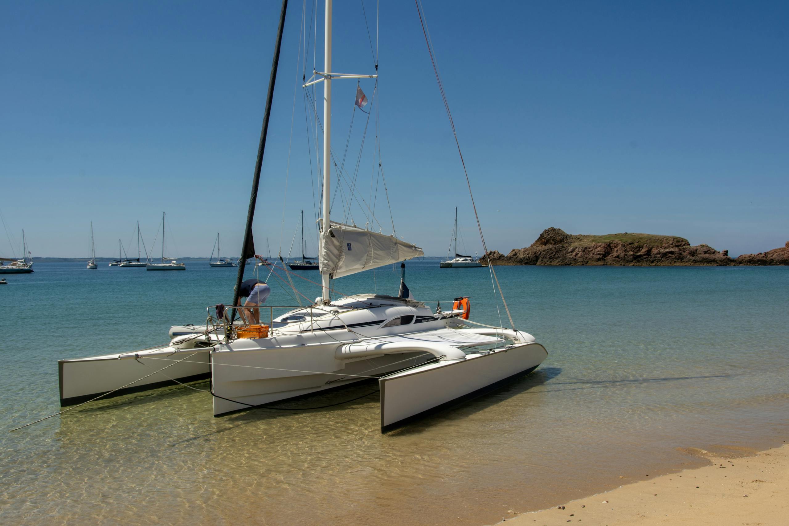 A sailing catamaran rests on a sandy beach with clear blue water under a sunny sky.